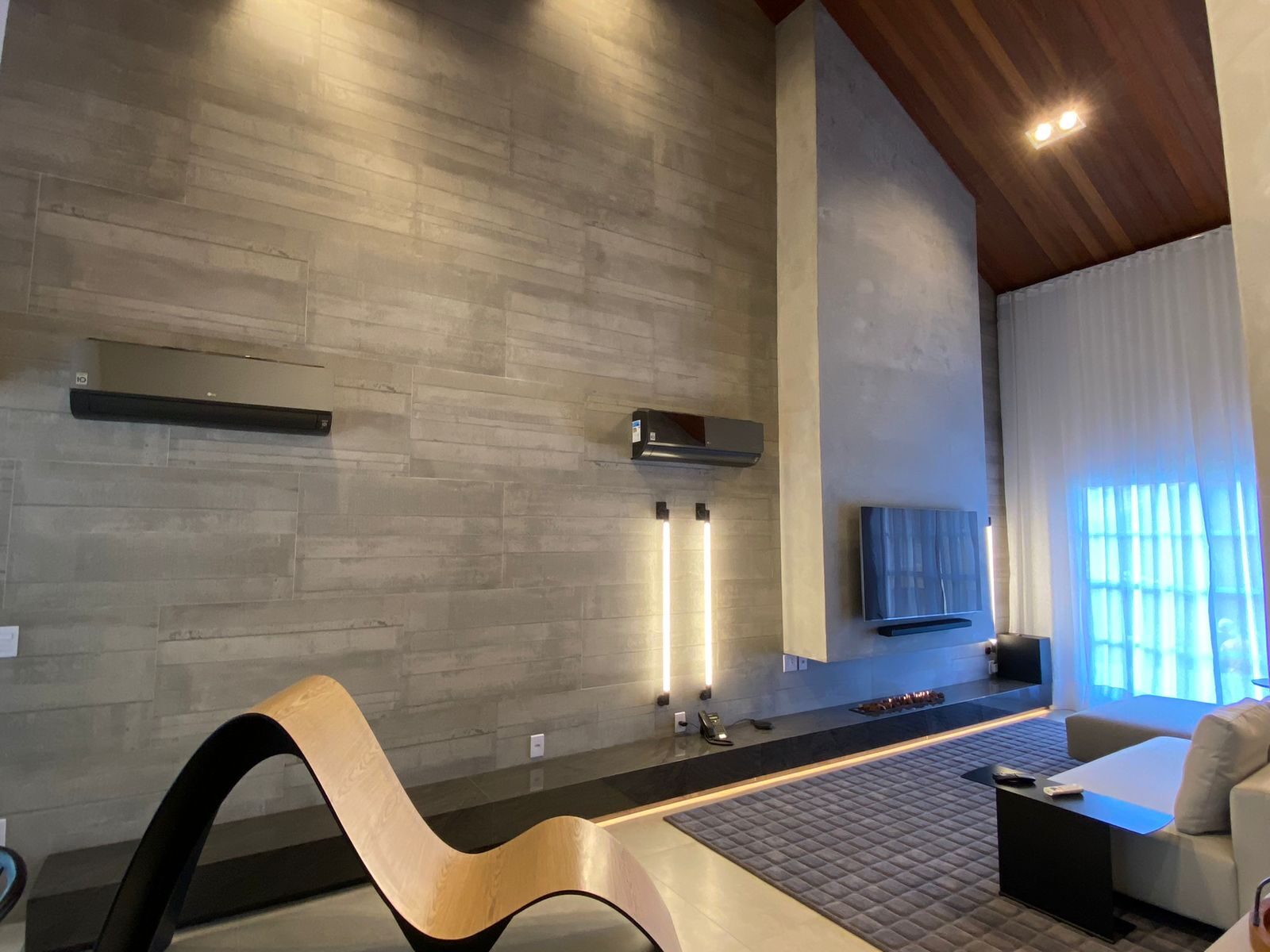 Sala de estar com parede em porcelanato canjiquinha e pé-direito duplo