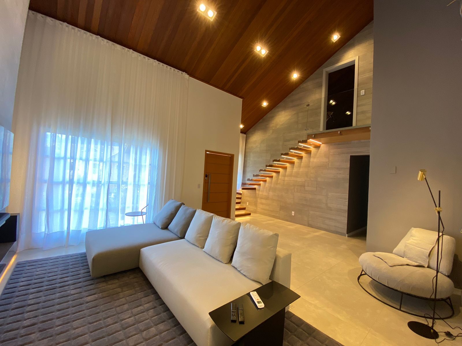Escada suspensa em madeira sobre parede de porcelanato, integrada ao living